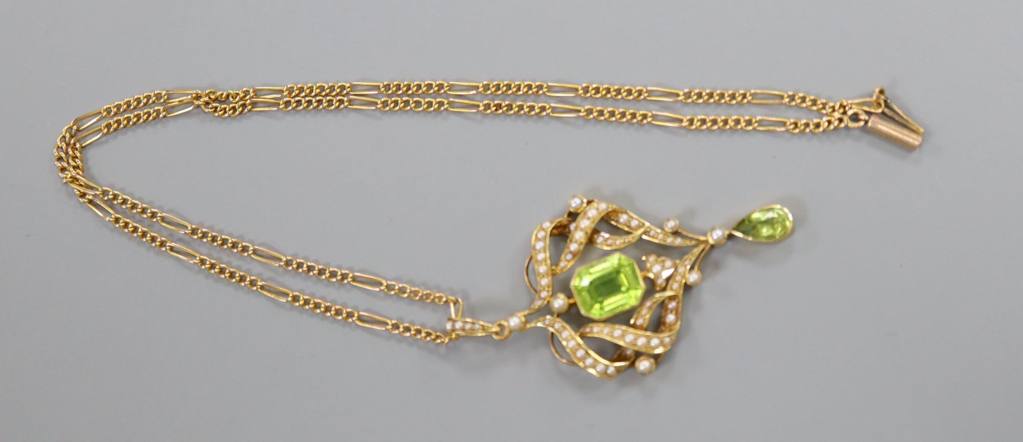 An Edwardian gold, seed pearl and two stone peridot set scroll pendant, overall 53mm, gross 7.4 grams, on 9ct chain.